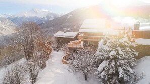 Un centro turístico de montaña cubierto de nieve, con edificios de madera y una vista despejada de montañas nevadas al fondo.
