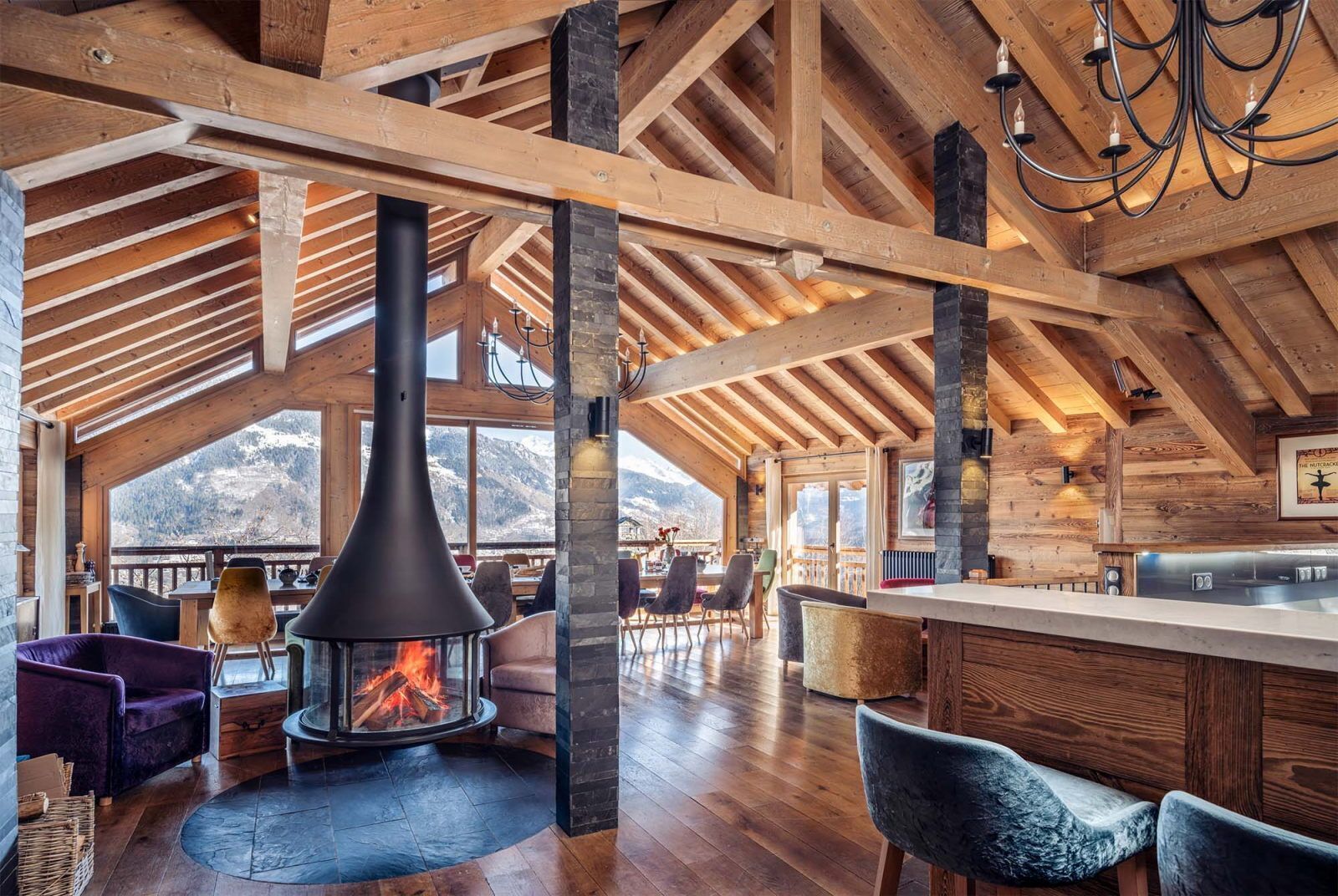 Una habitación amplia con techo alto, vigas de madera, chimenea y vistas a montañas.