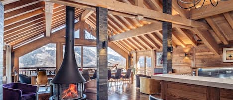 A spacious room with a high ceiling, wooden beams, a fireplace, and a view of mountains.