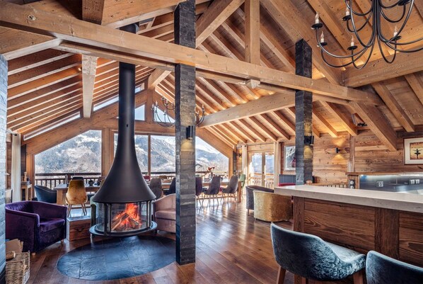 A spacious room with a high ceiling, wooden beams, a fireplace, and a view of mountains.