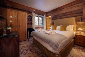 Un dormitorio con una cama grande, cabecera de madera, una mesita de noche con lámpara, un armario y una ventana con cortinas.