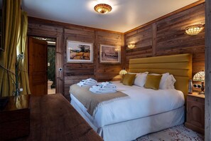 Ein Schlafzimmer mit einem hölzernen Kopfende, einem Bett mit weißen Leinen, zwei Wandlampen und einem gerahmten Landschaftsbild.
