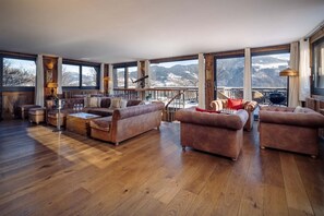 A spacious living room with large windows, a wooden floor, and a view of mountains.