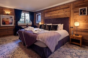 Habitación de hotel con una cama grande, cabecera de madera, mesita de noche con lámpara y ventana con cortinas.