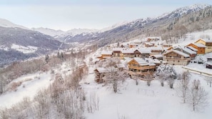 A snow-covered mountain village with wooden chalets, a ski slope, and a valley.