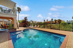 A swimming pool with lounge chairs, a covered seating area, and a fenced garden.