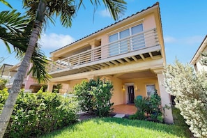 A two-story building with a balcony, a door, and a small garden area.