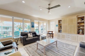 A spacious living room with a large window, a ceiling fan, and a built-in cabinet with decorative items.