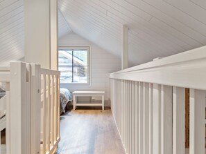 Un couloir étroit avec un plafond en pente, une fenêtre donnant sur l’extérieur et un banc blanc.