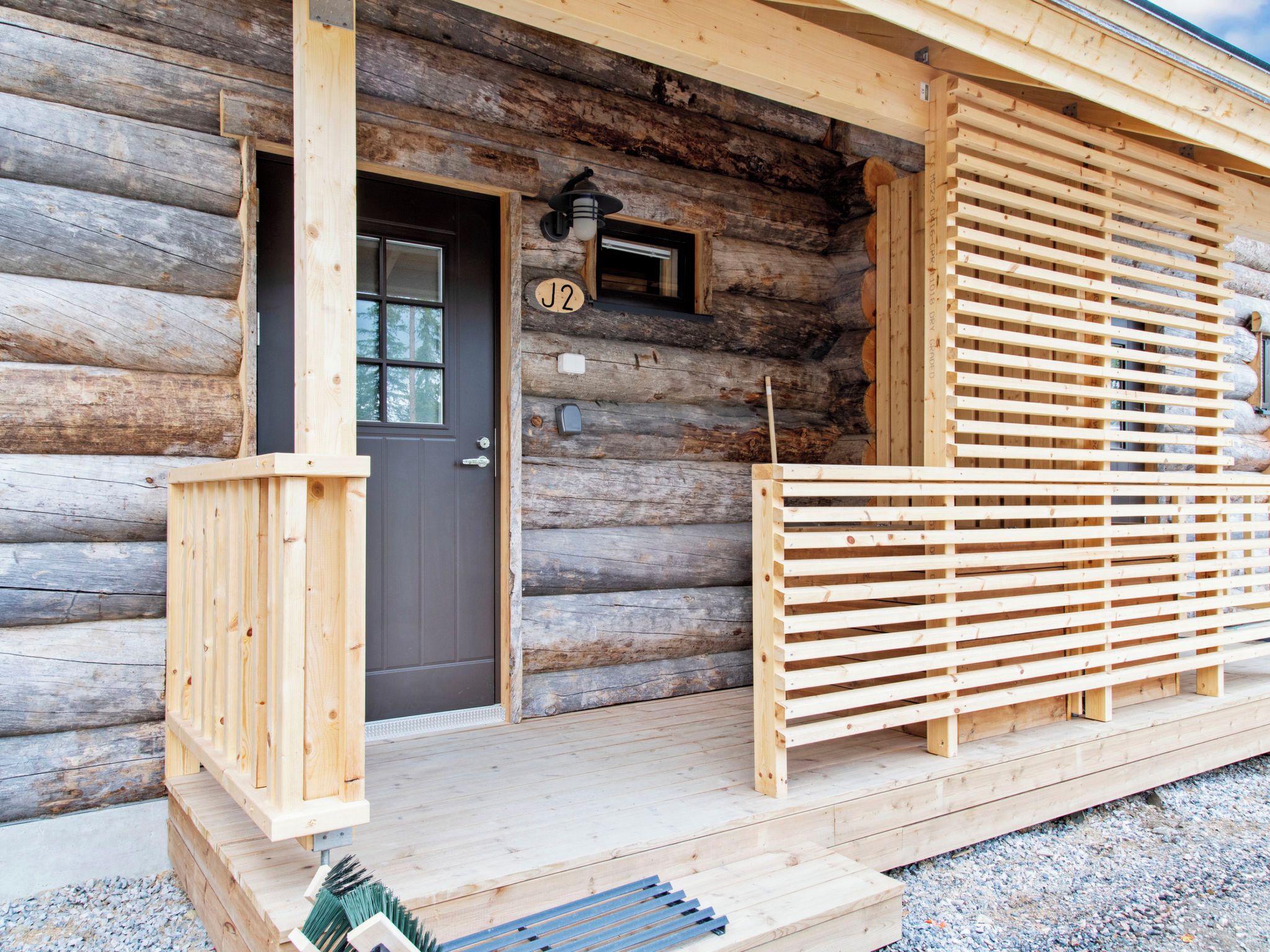 A log cabin with a wooden porch, a dark door, and a number plaque.