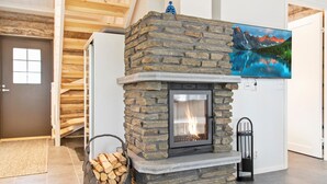 A stone fireplace with a fire, a basket of firewood, and a painting of a mountain landscape.