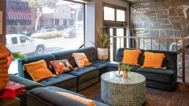 A modern lounge area with a large window, a blackboard with a map, and a seating arrangement with orange cushions. - Samesun San Francisco - Hostel (San Francisco)