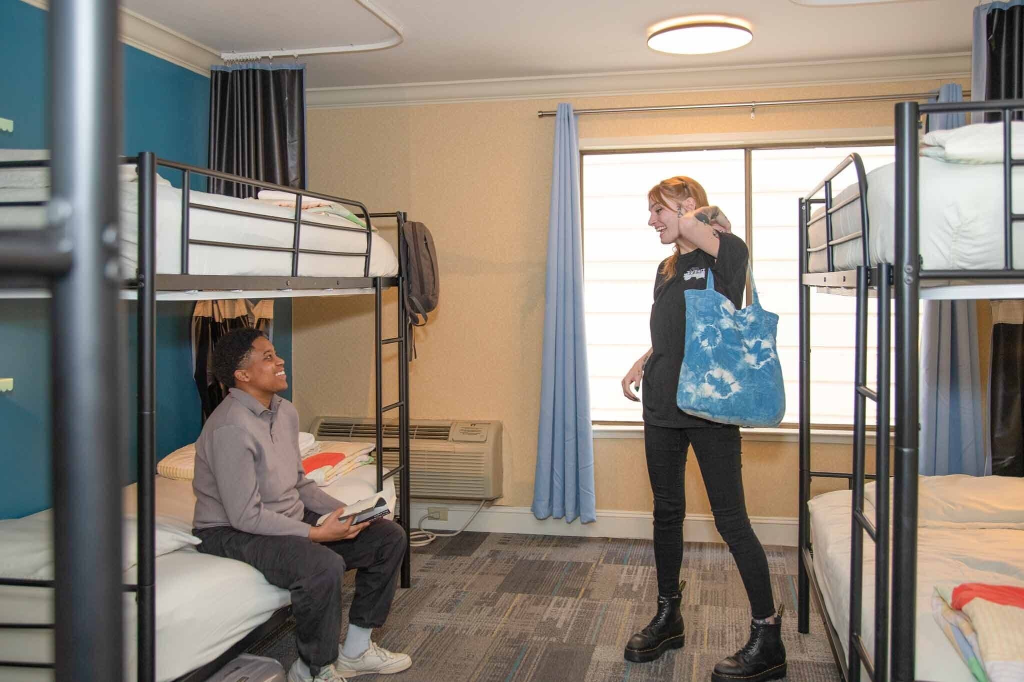 A dormitory room with bunk beds, a window with curtains, and a radiator.