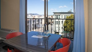 A room with a large window, a table with chairs, and a view of buildings and mountains. - Samesun San Francisco - Hostel (San Francisco)