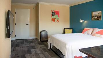 Hotelkamer met een bed, bureau, stoel, koffer, deur en een muur met een schilderij.