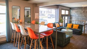 A modern hotel lobby with a glass table, orange and white chairs, a grey sofa with orange cushions, and a map on the wall. - Samesun San Francisco - Hostel (San Francisco)