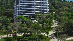 Un hotel de gran altura con una cúpula central y varios pisos, rodeado de abundante vegetación y una vista despejada del océano.