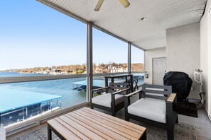 A balcony with a view of a body of water, a grill, and seating area.