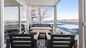 Een modern terras buiten met een bank en tafel, grote ramen bieden uitzicht op een gebouw en landschap.