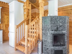 A wooden staircase leading to a second floor, a white refrigerator, and a stone fireplace. - Tinttityy by Interhome (Nilsiä)