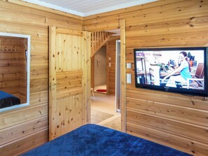 A wooden interior with a bed, a television mounted on the wall, and a staircase leading to another room.