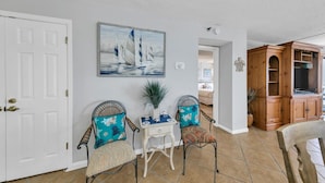 A room with two wicker chairs with blue and red patterned cushions, a small white table with a vase and a plant, and a wooden cabinet with a TV. - Remodeled Beachfront beauty! Inlet Reef 416 (Destin)