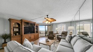A spacious living room with a large gray sofa, wooden entertainment center, and a ceiling fan. - Remodeled Beachfront beauty! Inlet Reef 416 (Destin)