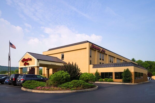 A Hampton Inn with a yellow facade, a covered parking area, and a landscaped entrance.