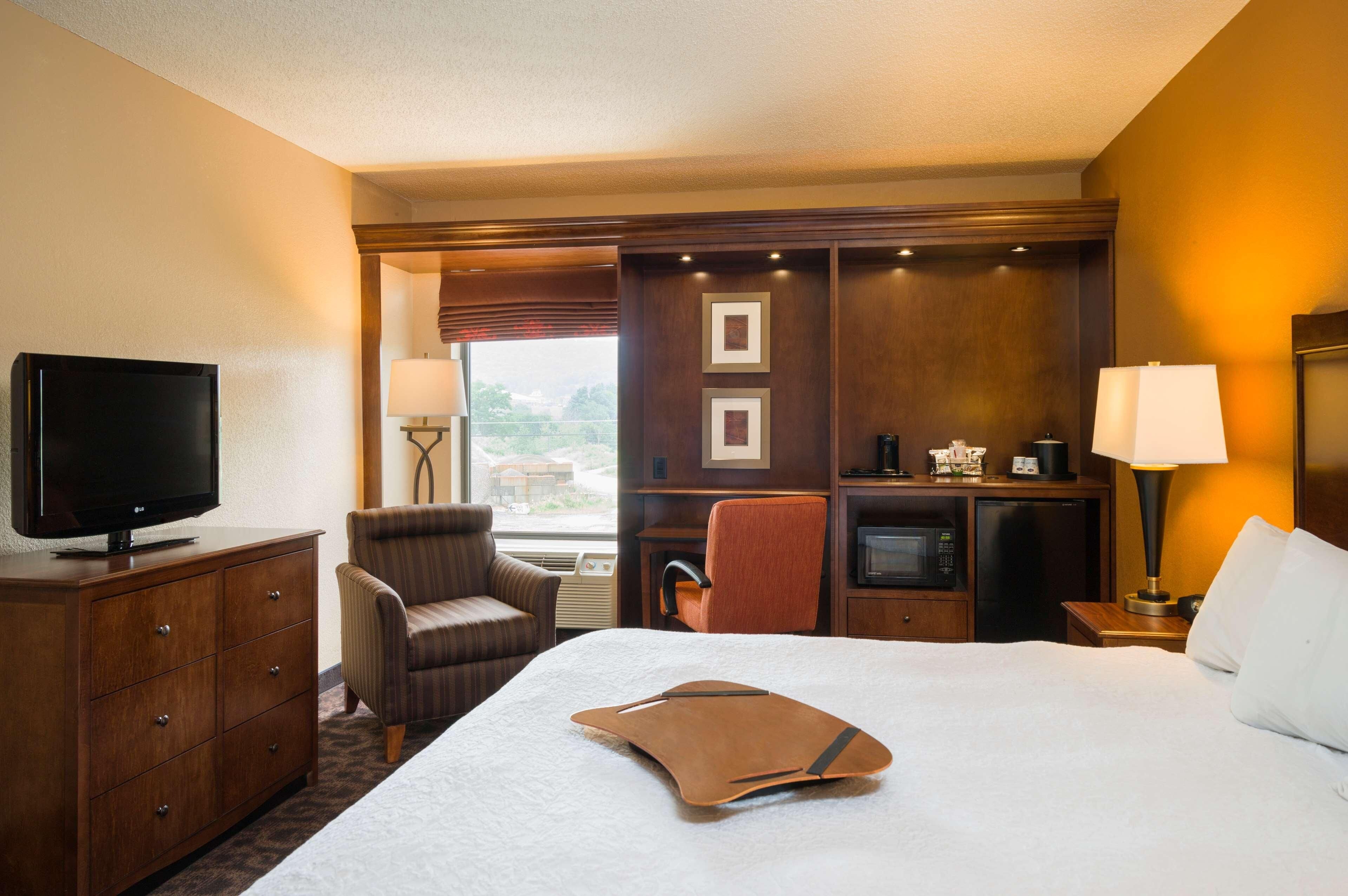 A hotel room with a bed, a television, a desk with a computer, a chair, and a window with a view.