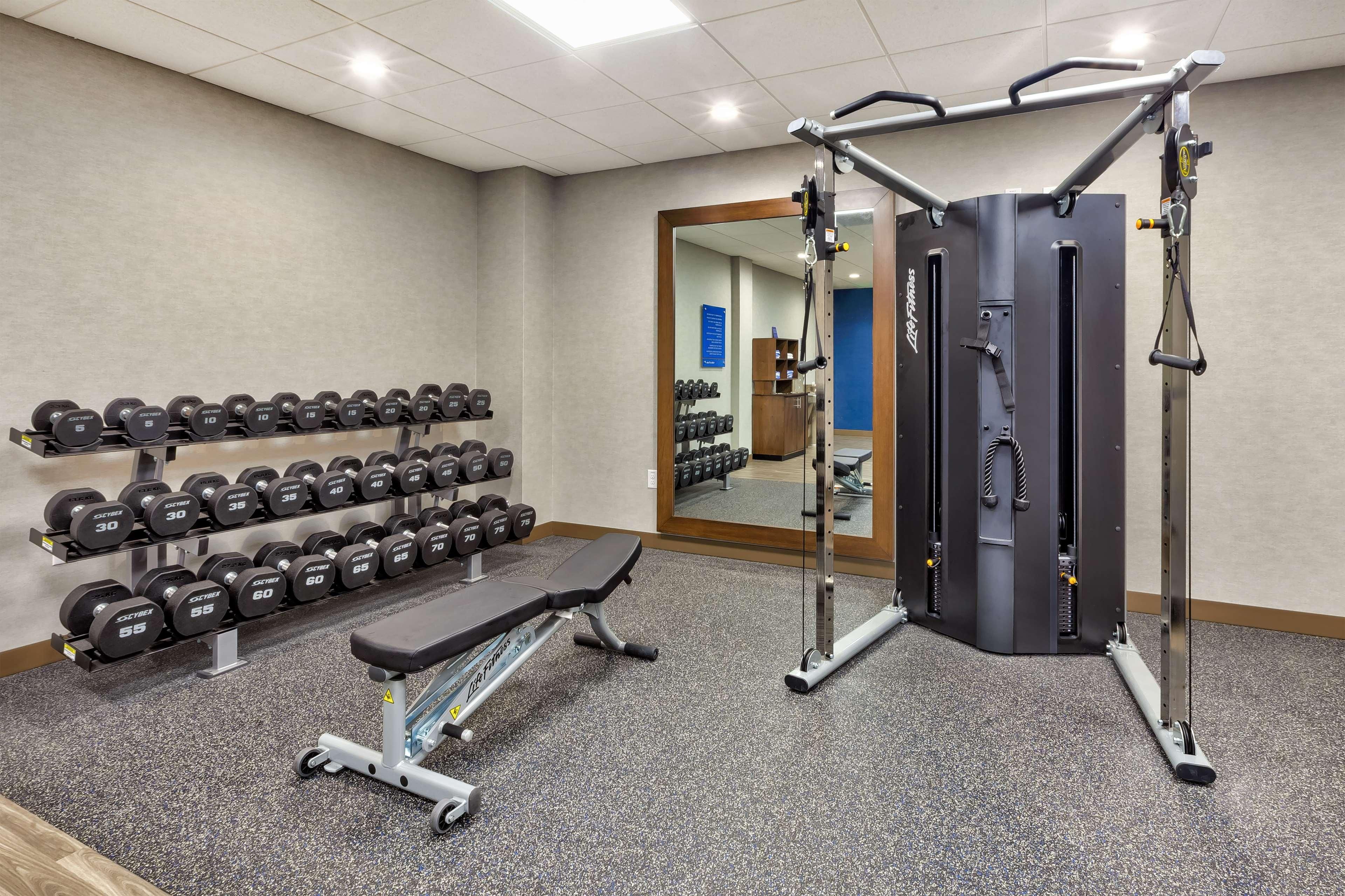 A gym with weight racks, dumbbells, a bench, and a cable machine.