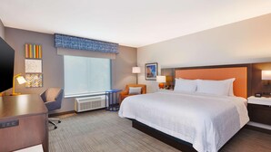 Habitació d'hotel amb un llit gran, una taula de treball, una cadira, una finestra i obra d'art a les parets.