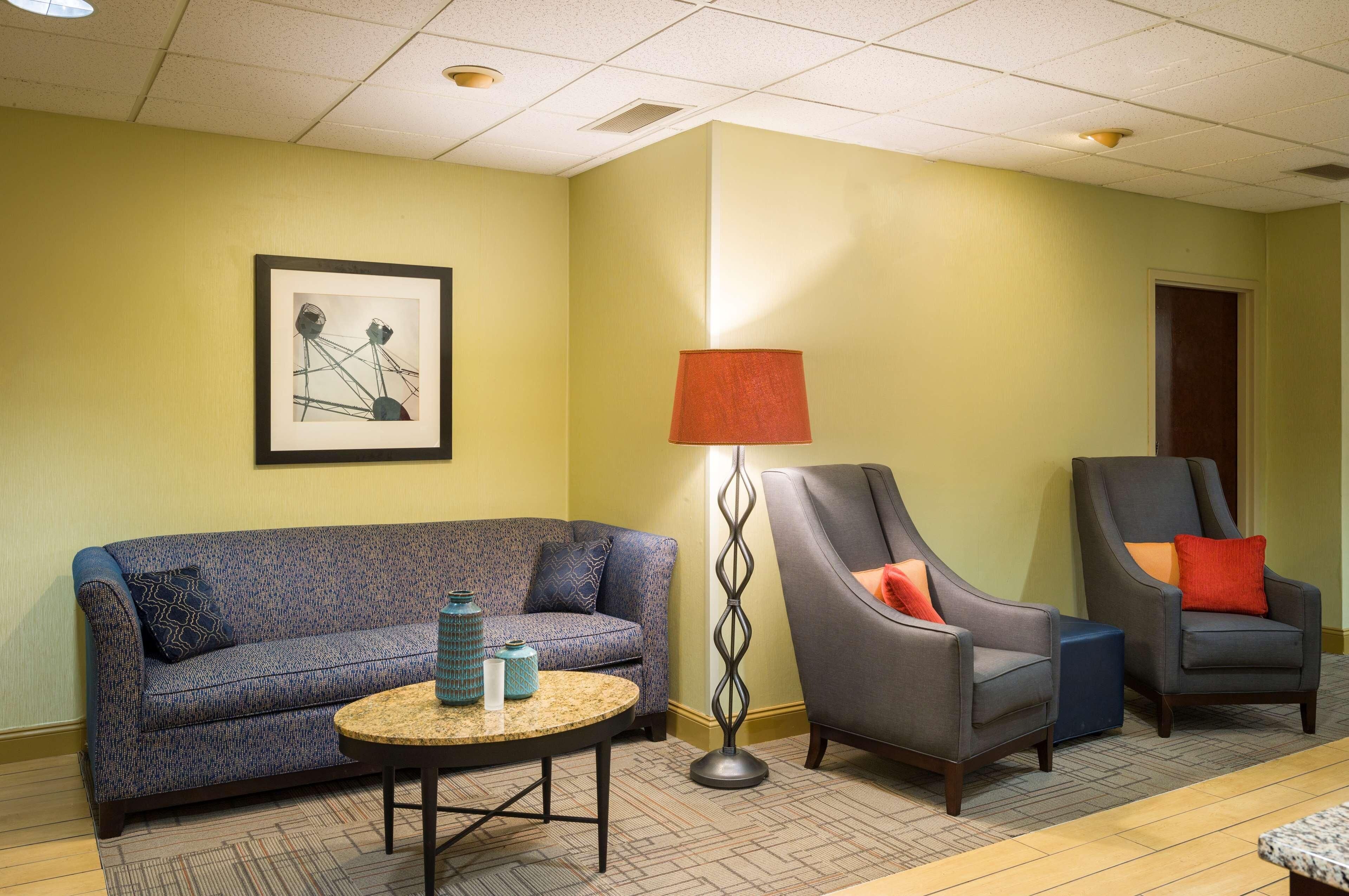 A hotel lobby with a sofa, two armchairs, a floor lamp, and a framed artwork on the wall.