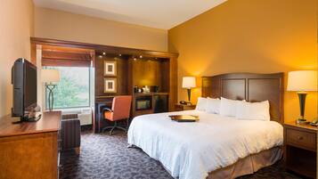 Une chambre d’hôtel avec un grand lit, un bureau avec une télévision, une chaise, une lampe de bureau et une table de chevet avec une lampe.
