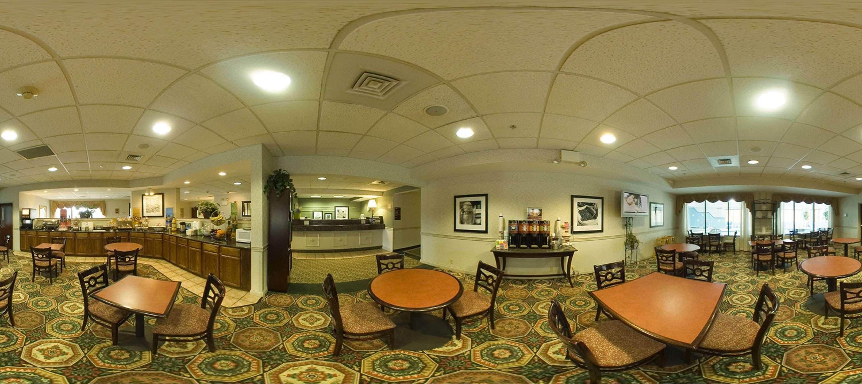 A spacious hotel lobby with a central bar, multiple dining tables, and patterned carpet flooring.