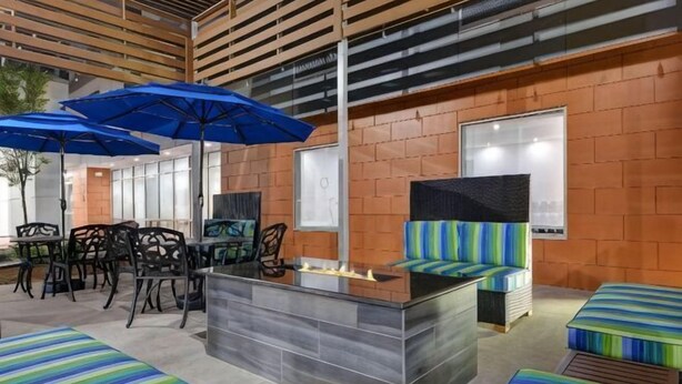 A bar area with seating, a counter, and blue umbrellas. - Home2 Suites by Hilton Bentonville Rogers (Bentonville)