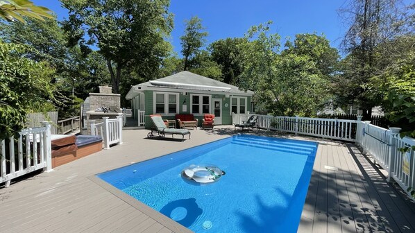 Um quintal com piscina, cadeiras de deck e um pequeno edifício com chaminé.