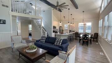 A spacious living area with a blue sofa, striped armchairs, a coffee table, and a dining area with a chandelier.