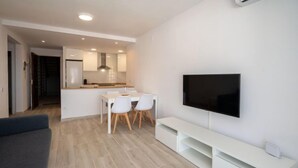 A modern living room with a flat-screen TV, a dining area with a table and chairs, and a kitchen in the background. - Blue Sea by Interhome (Cunit)