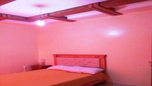 Una cama individual con cabecera de madera en una habitación con paredes rosas y un travesaño de madera en el techo.