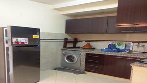 Una cocina compacta con refrigerador de acero inoxidable, lavadora y gabinetes de madera oscura.