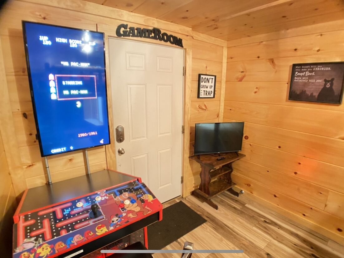 Una habitación con una consola de videojuegos, un televisor y una puerta con la leyenda 'CAMEROUN'.