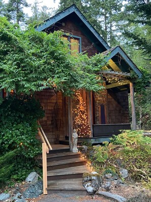 Eine rustikale Holzhütte mit einer Holztreppe, die zu einer Veranda führt, umgeben von dichtem Grün.