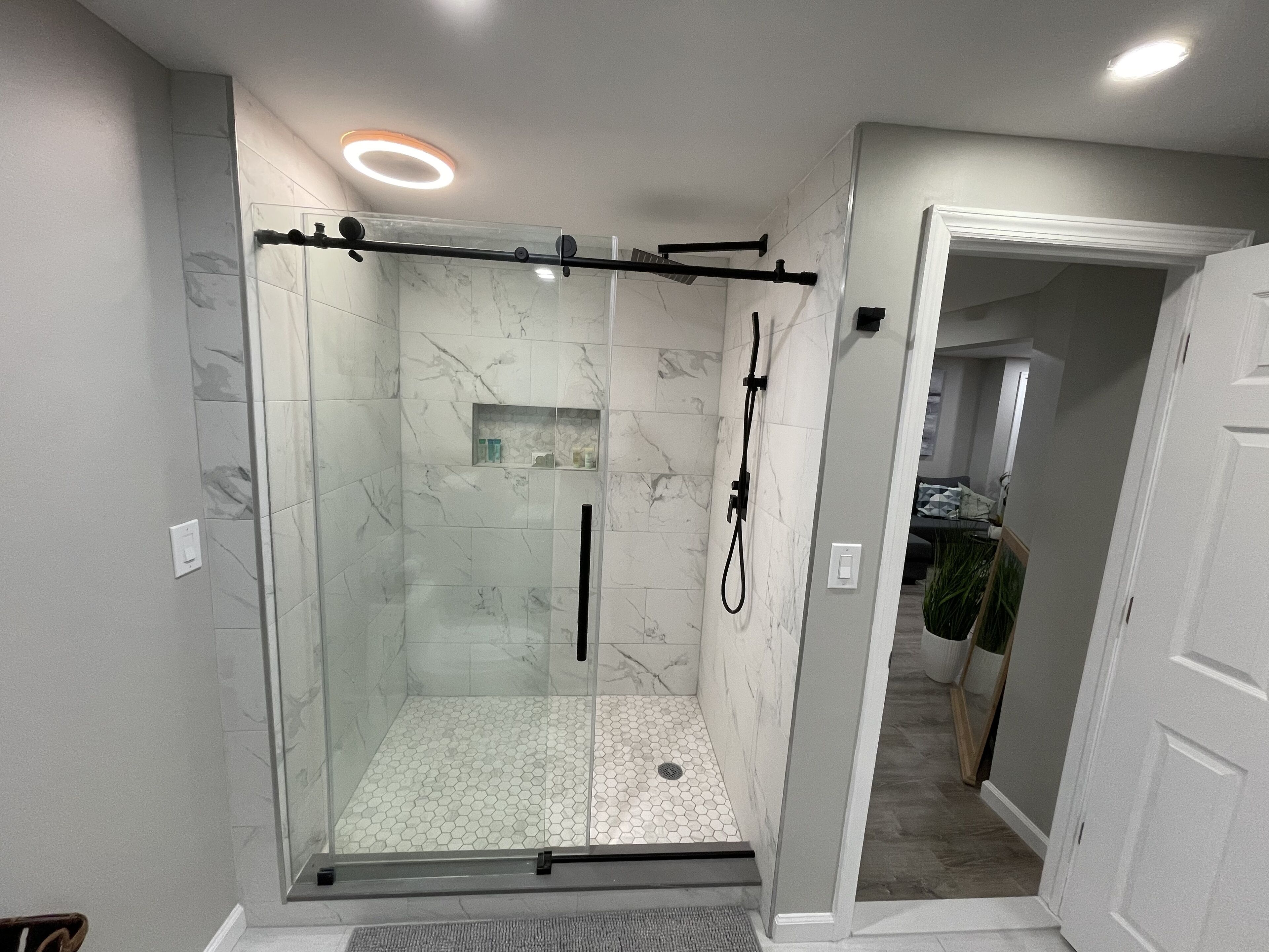 A modern shower with glass doors, a handheld showerhead, and a built-in shelf.