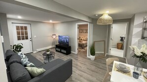 Una sala de estar moderna con un sofá gris, un televisor y un comedor con una mesa dispuesta para dos.
