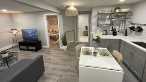 Una cocina moderna con comedor, un televisor en la sala de estar y un pasillo que conduce a un dormitorio.