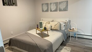 Un dormitorio con cama, mesita de noche y una silla pequeña. Hay tres obras de arte colgadas en la pared sobre la cama.