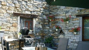 A stone wall with a grill, outdoor table, chairs, and potted plants.