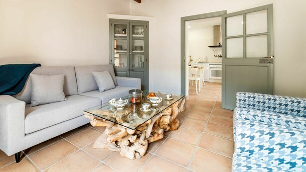 A living room with a glass coffee table, grey sofa, and a patterned sofa. A wooden cabinet with glass doors is visible in the background. - Wonderful private villa for 6 people with WIFI, A/C, TV and patio (Andratx)