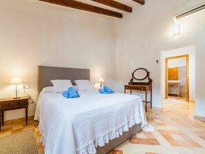 Un dormitorio con una cama grande, dos mesitas de noche con lámparas, un aparador de madera y un baño visible a través de una puerta abierta.