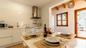 A modern kitchen with white cabinetry, a stainless steel range hood, and a dining area set for a meal with plates, glasses, and a bottle of wine. - Wonderful private villa for 6 people with WIFI, A/C, TV and patio (Andratx)